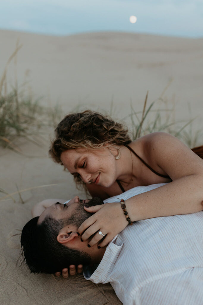 Couple laying down on the beach together with the moon in the background