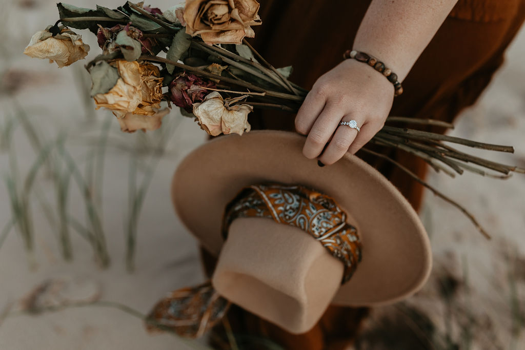 Woman holding her hat and dried florals during her engagement shoot