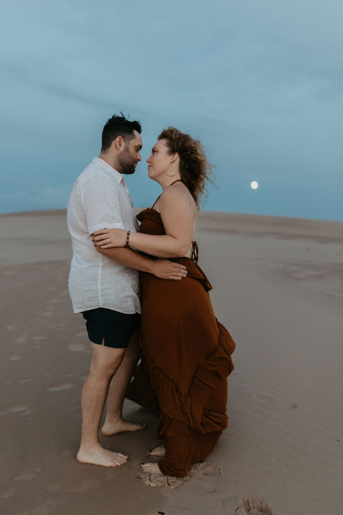 Couple posing during their Silver Lake Sand Dunes engagement photos with the moon in the backdrop