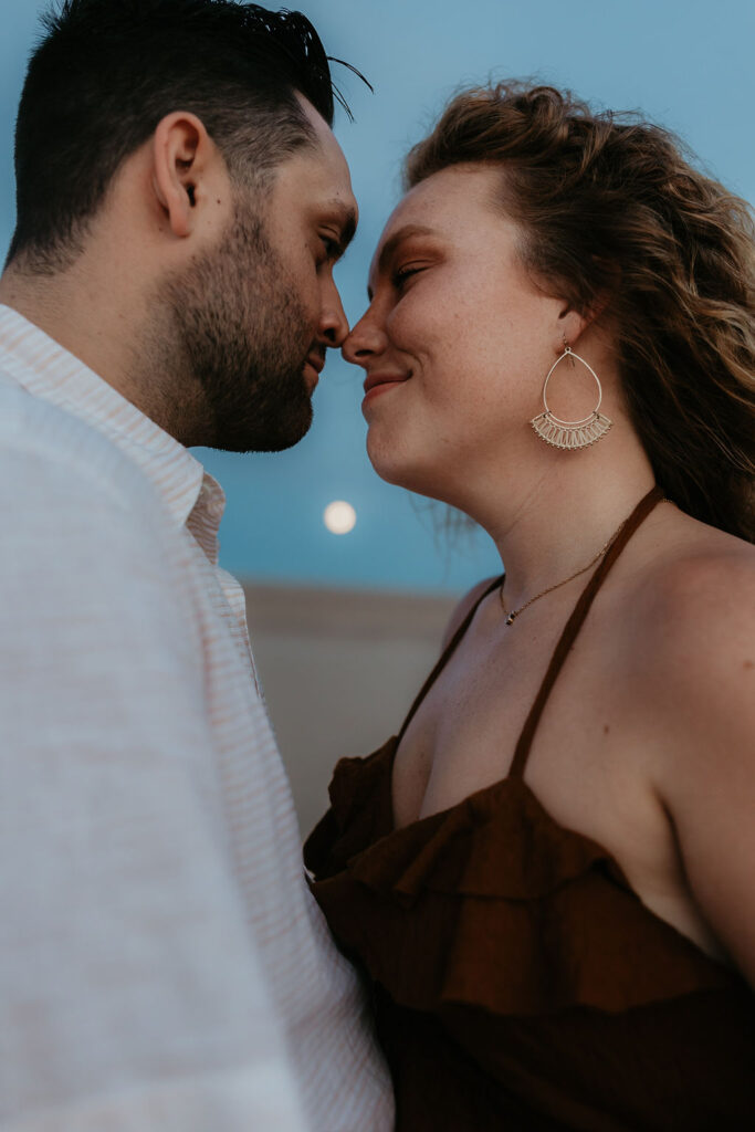 Couple posing during their Silver Lake Sand Dunes engagement photos with the moon in the backdrop