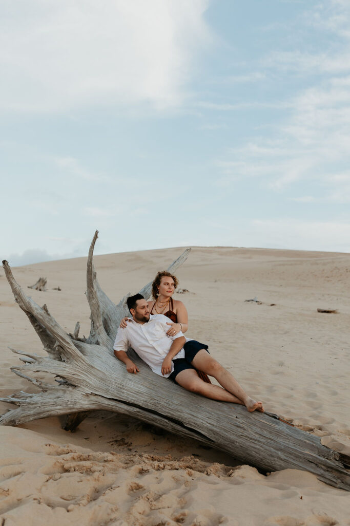 Couple posing on a piece of driftwood during their Silver Lake Sand Dunes engagement photos in MI