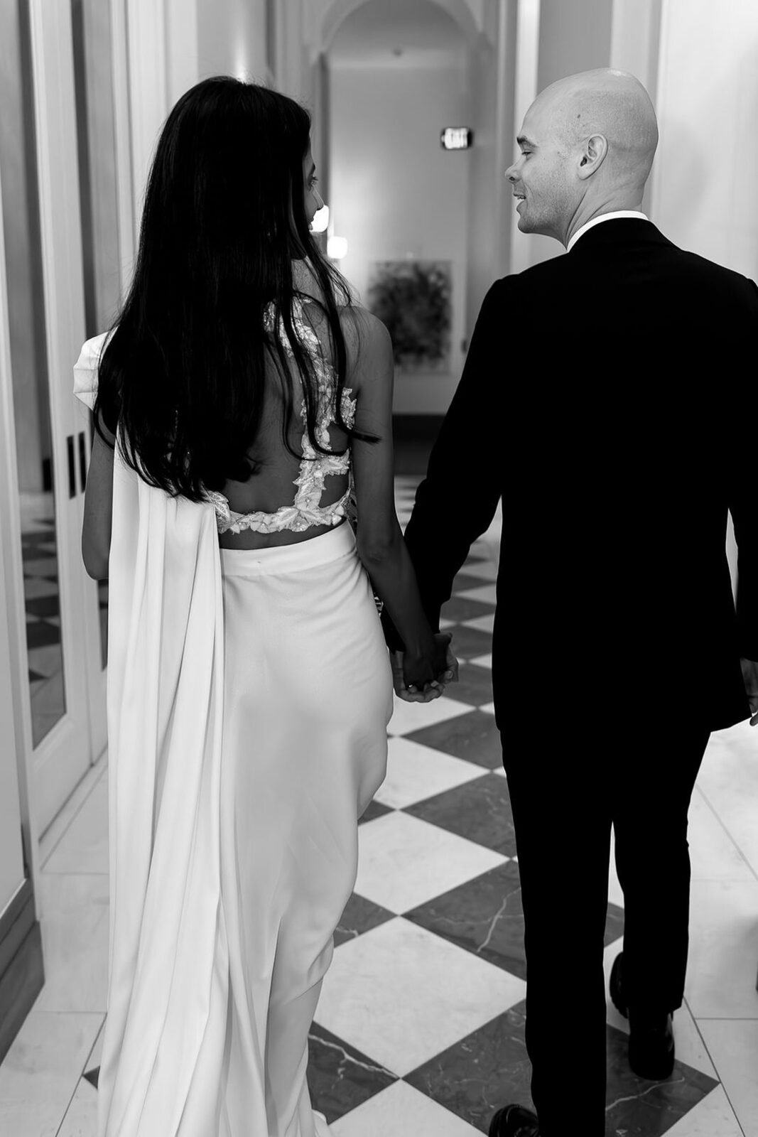 Black and white photo of a bride and groom walking down a hallway