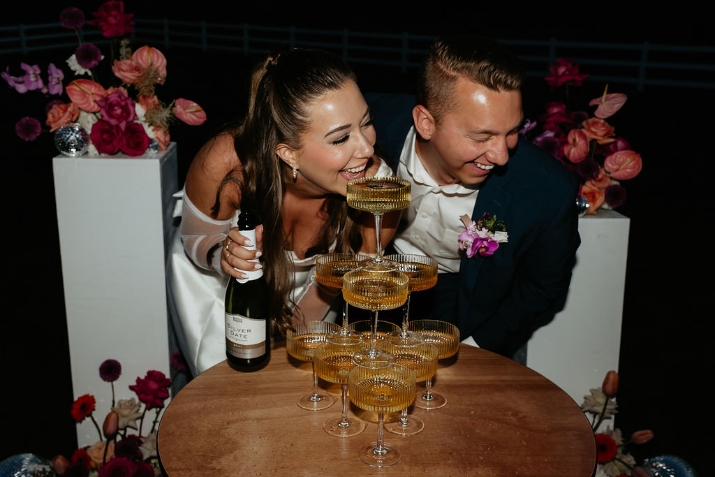 Bride and groom laughing as they drink from their champagne tower with wedding reception flash photos