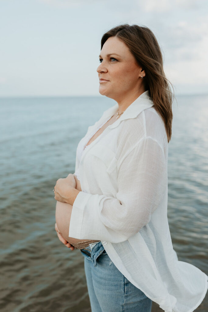 Mother holding her belly during her Michigan beach maternity photos on Lake Huron