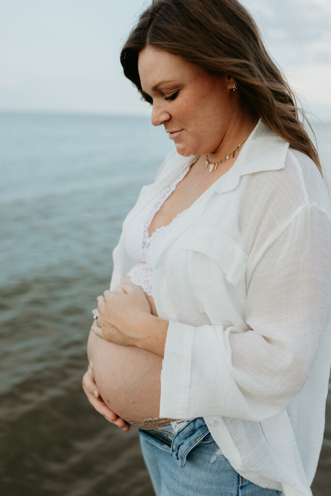 Mother holding her belly during her Michigan beach maternity photos on Lake Huron