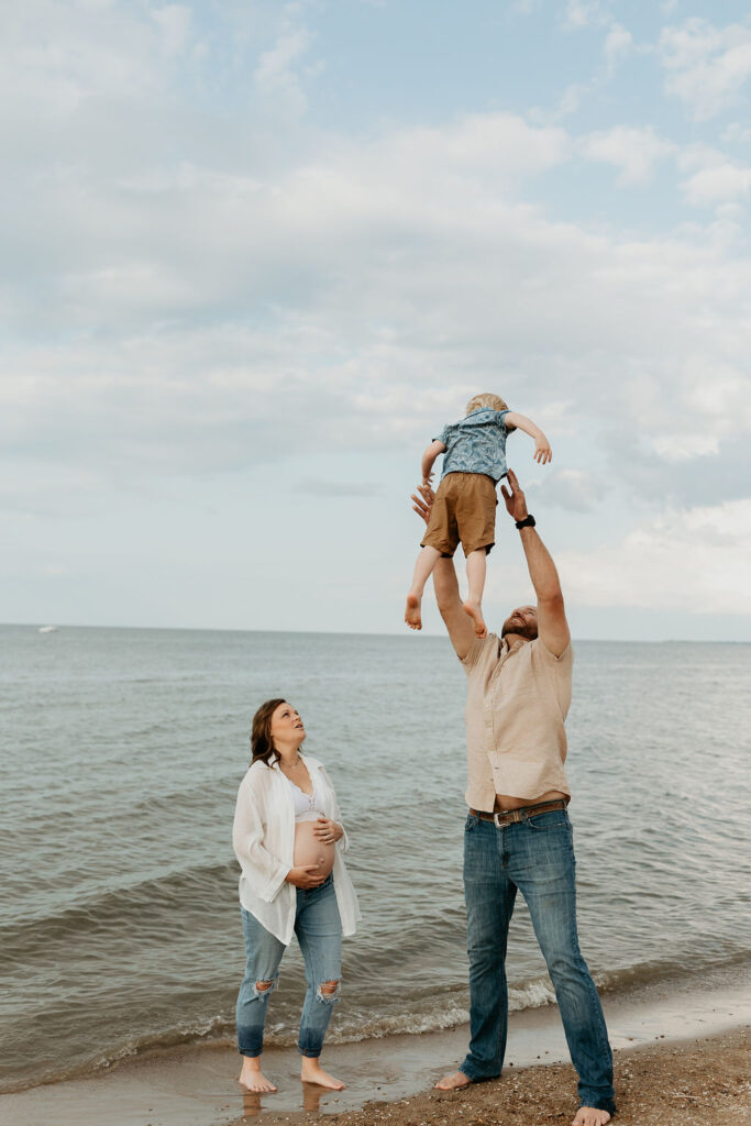 Father throwing son in the air during their Michigan beach maternity photos on Lake Huron