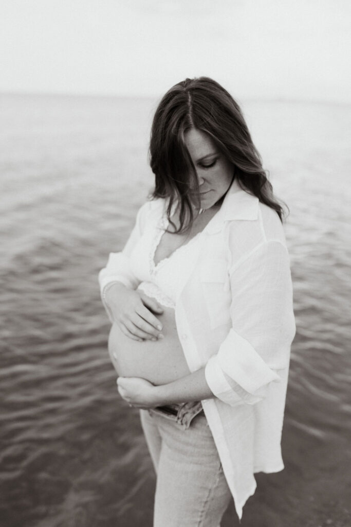 Mother holding her belly during her Michigan beach maternity photos on Lake Huron