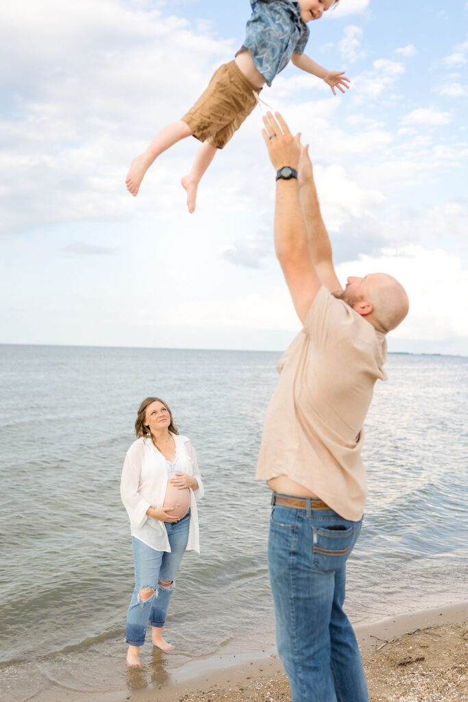 Father throwing son in the air during their Michigan beach maternity photos on Lake Huron